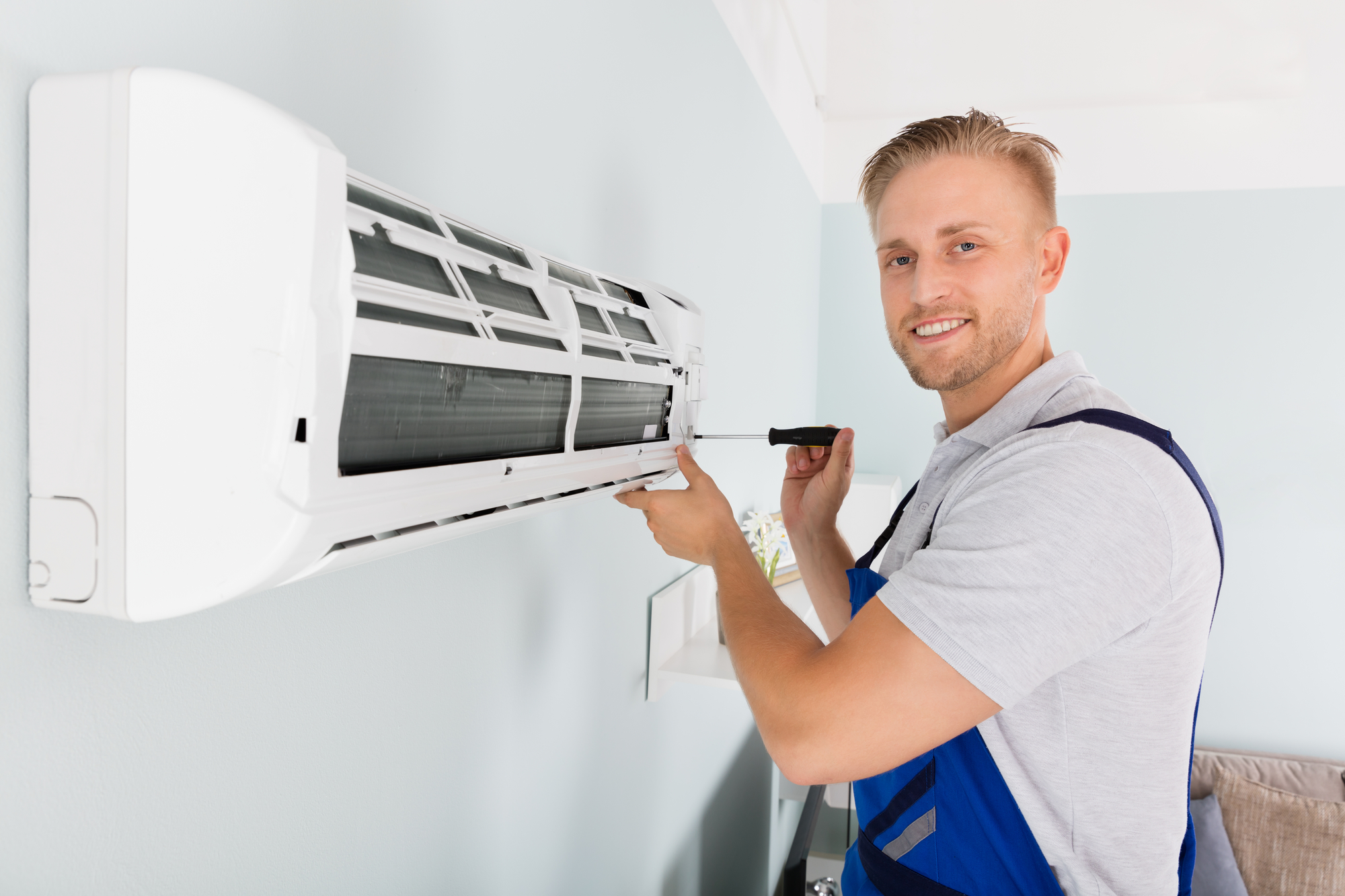 A man in overalls repairing an air conditioner.